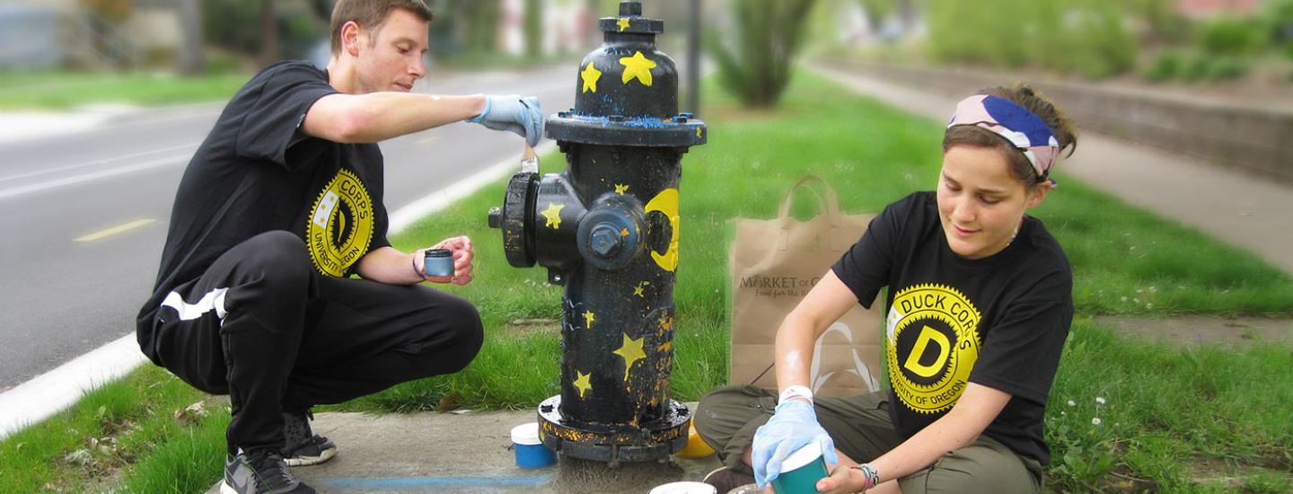 Duck Corps participants make a difference in the community. Two students painting a fire hydrant wearing Duck Corps t-shirts.